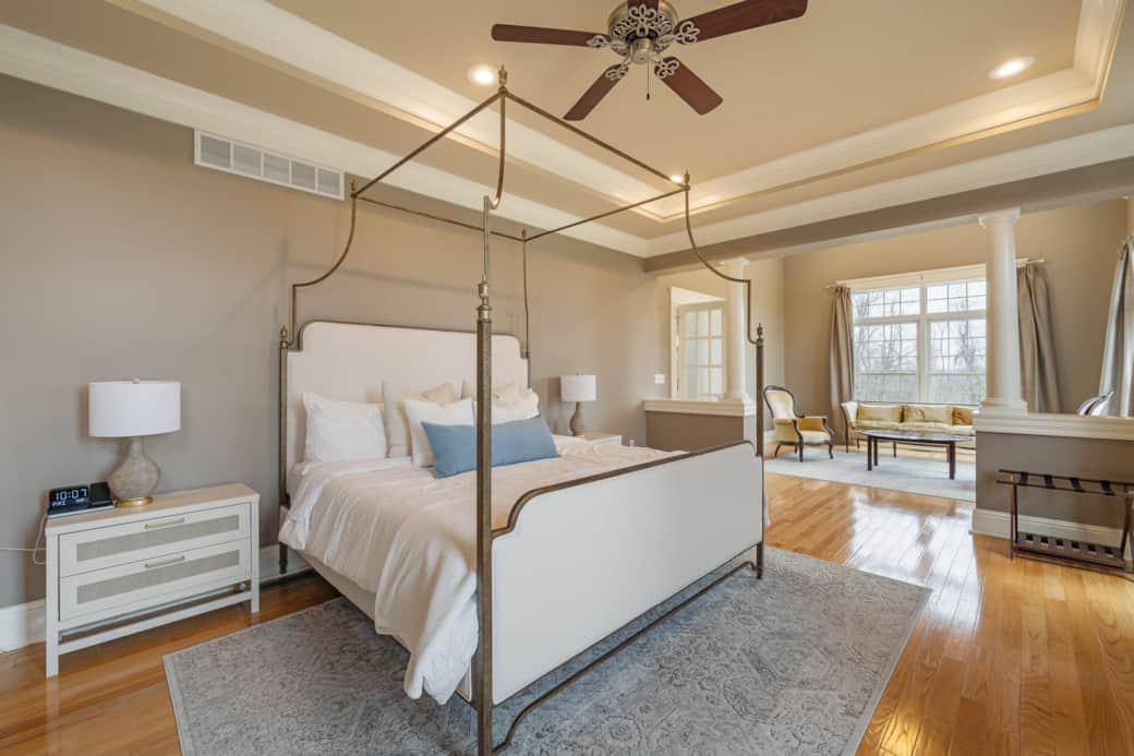 Spacious master bedroom with elegant king canopy bed, abundant natural light, and cozy sitting area.