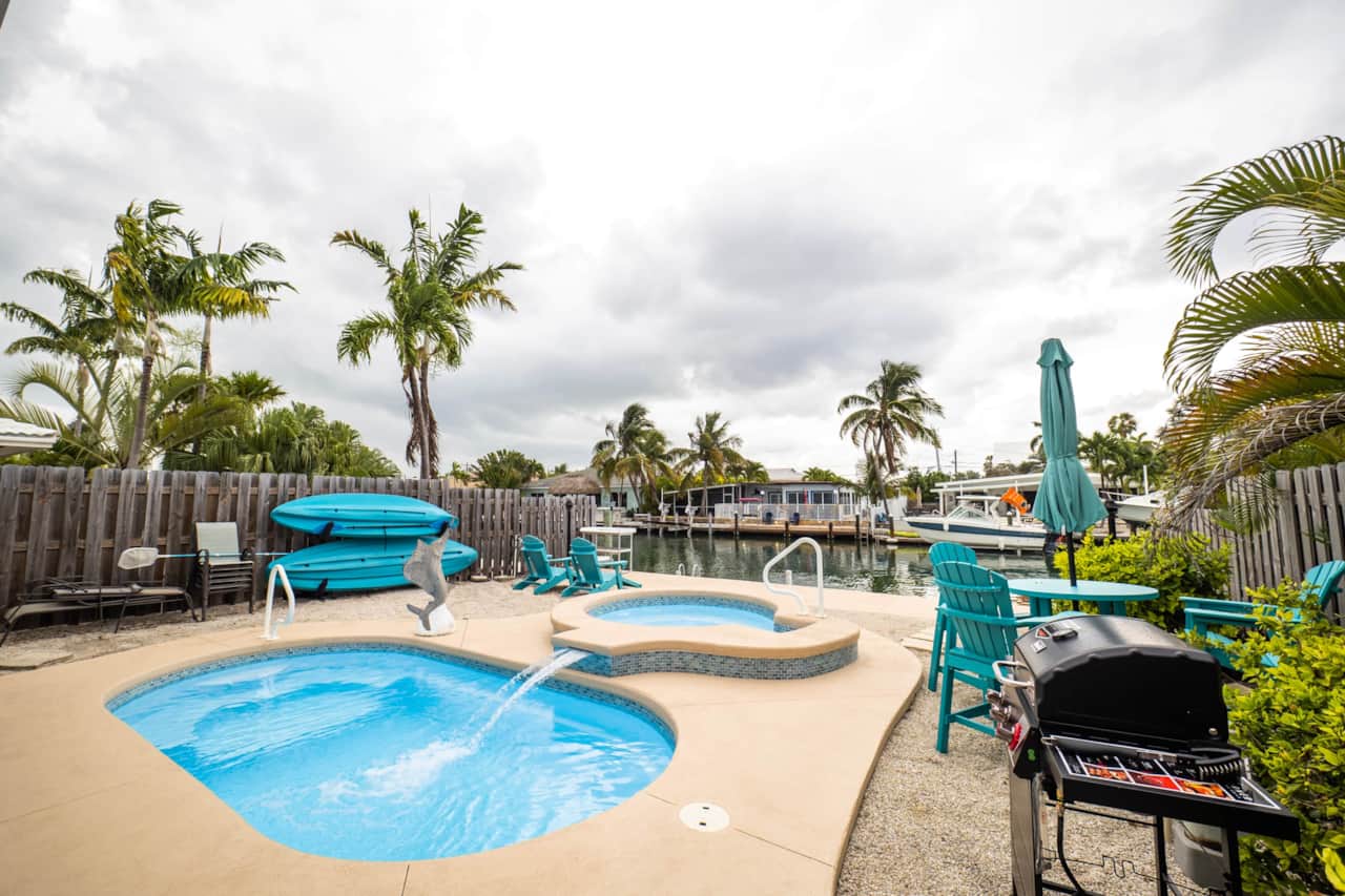 Heated private pool with a waterfall and hot tub, ringed by palms and loungers for all-day sun.