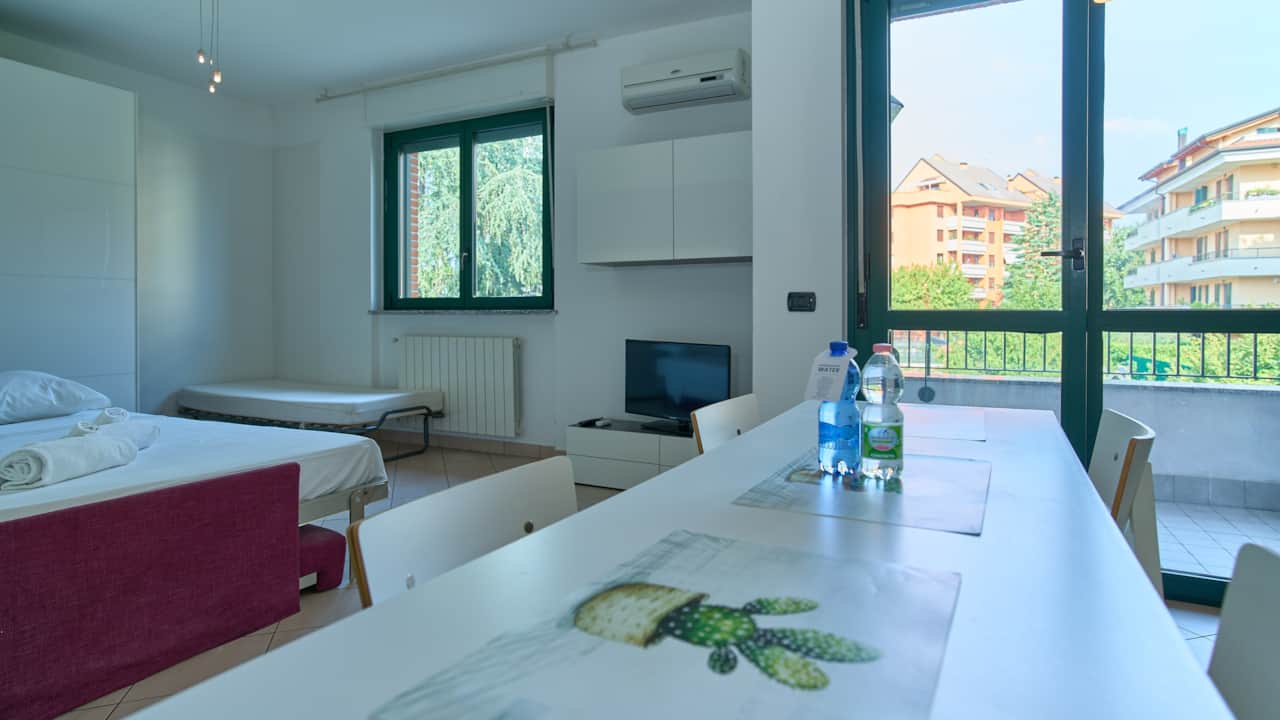 Mesa blanca con sillas y cama al fondo, en Monza
