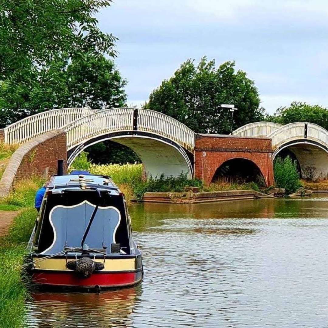 Holiday narrowboat moored in front of two white metal bridges