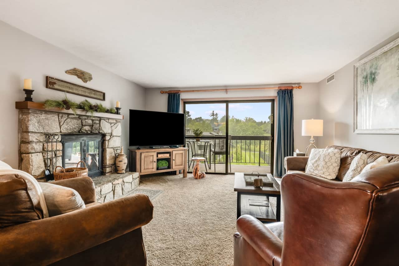 Cozy living room with stone wood-burning fireplace, Smart TV, and balcony access.  