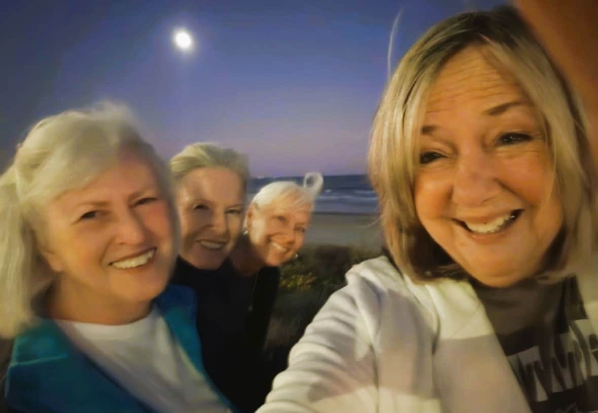 Four women smiling on the beach in Galveston celebrating a 25 year friendship tradition