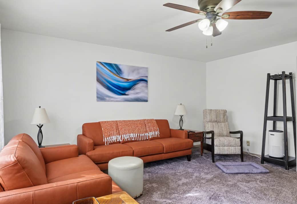 Living room with seating for 6, a recliner and a large Roku TV. Hallway to the bedroom on the right.