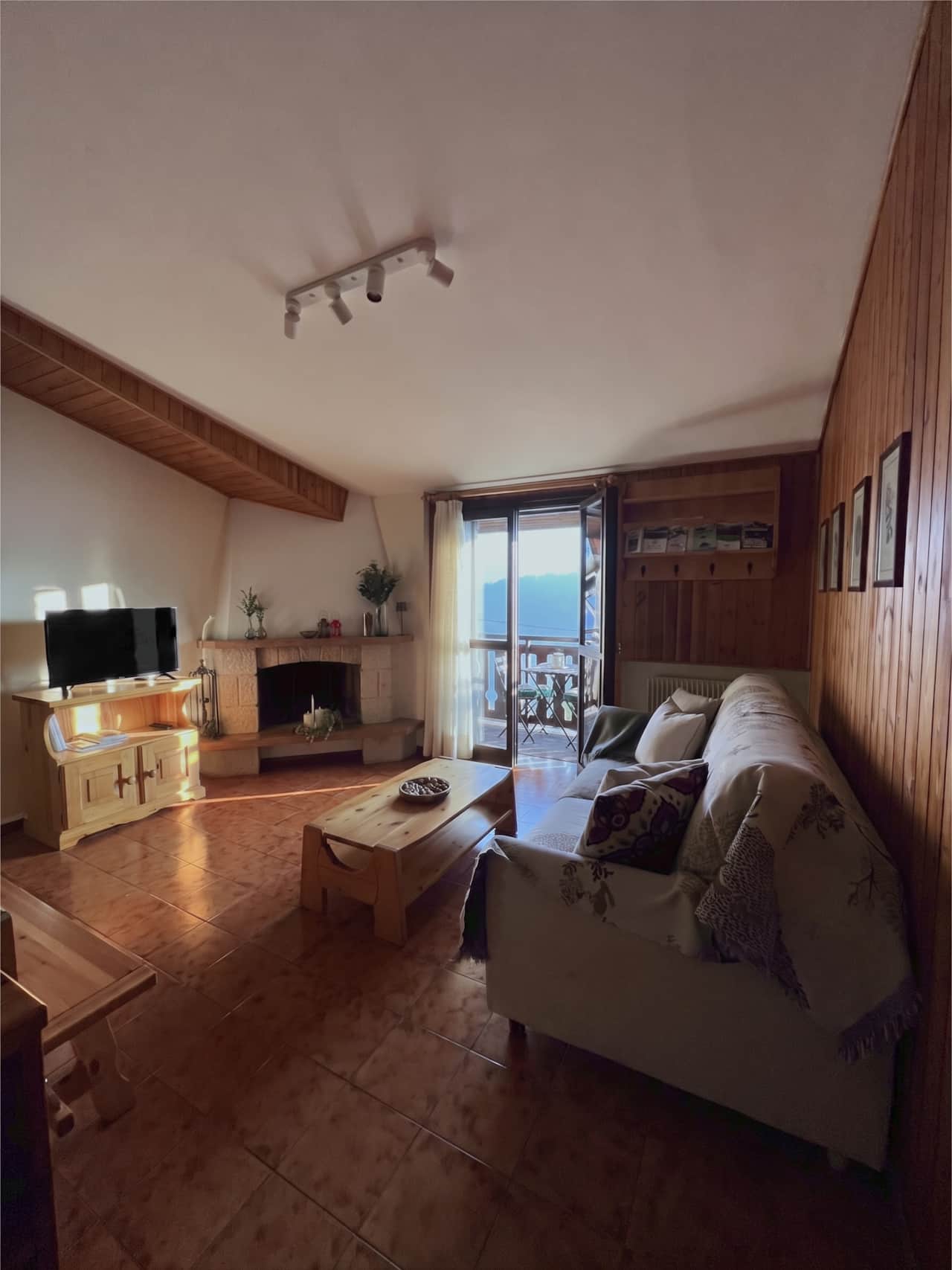 Soggiorno con TV, camino, divano e portafinestra sul balcone con vista sulle montagne