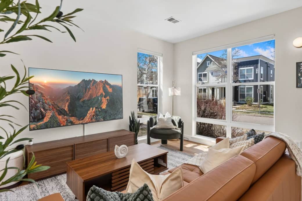 Sunlight pours in through large corner windows, creating a bright and inviting space to relax on the leather sofa or unwind with a movie after a day out.