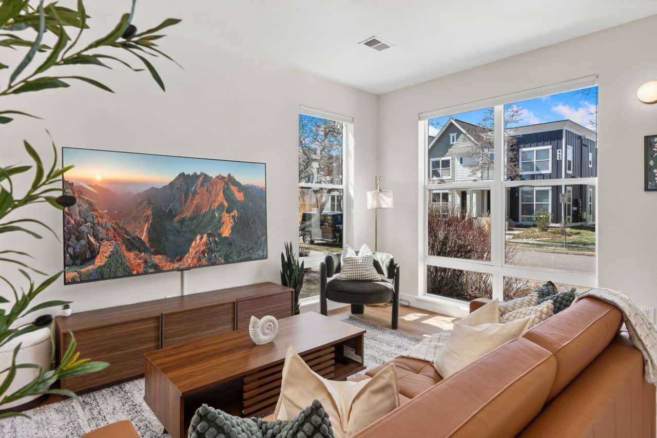 Sunlight pours in through large corner windows, creating a bright and inviting space to relax on the leather sofa or unwind with a movie after a day out.