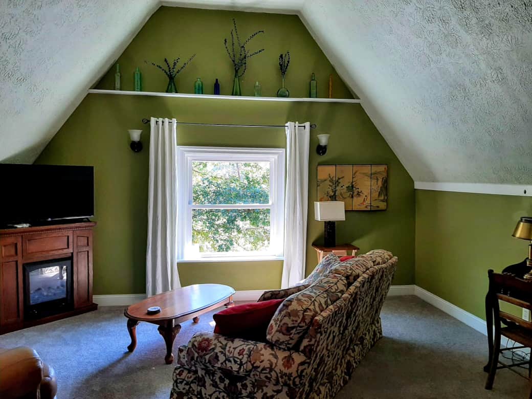 A large vaulted living room with Roku TV, electric fireplace, comfy sofa and chair and writing desk.