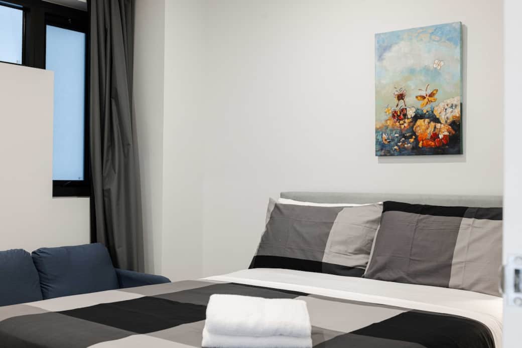 Experience comfort in our tastefully designed bedroom. The queen bed, with its striking gray and white bedding, is complemented by a vibrant wall art. The room's clean lines and modern decor ensure a restful night's sleep and a pleasant morning.