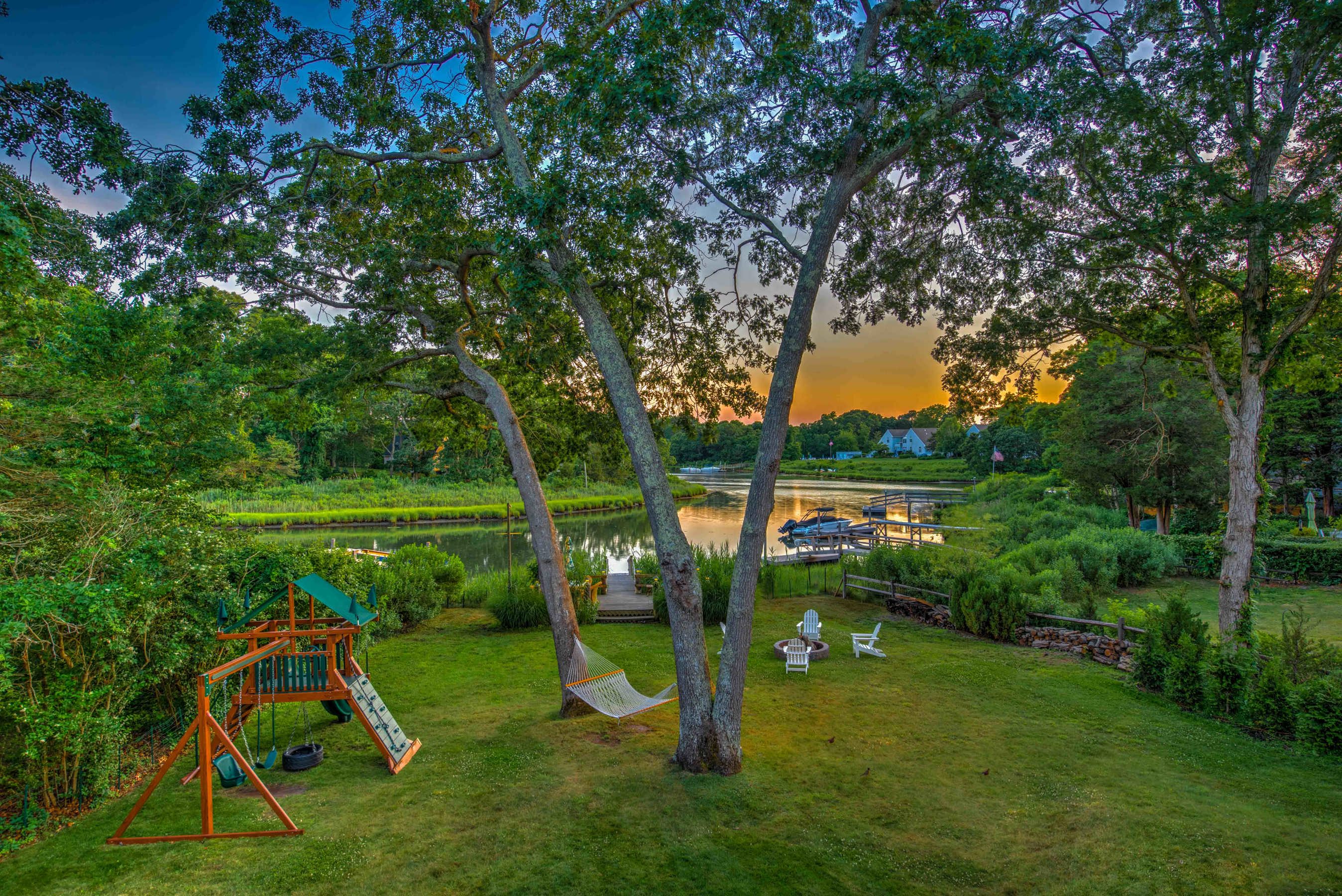 Backyard at sunset with playset, hammock and Adirondack chairs above the cove