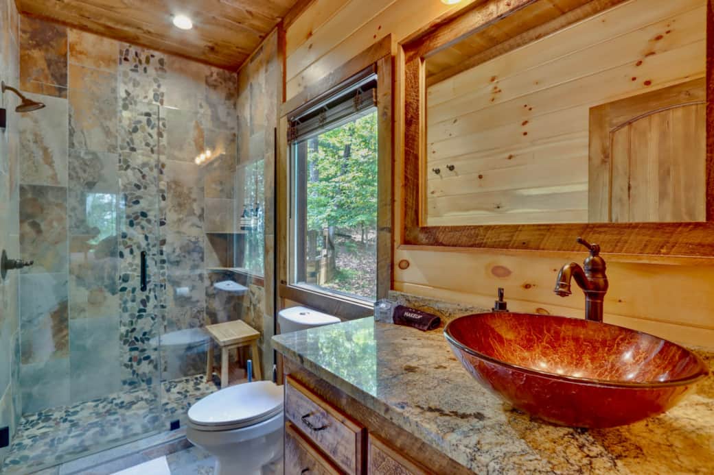 Master bath with stone shower, forest views, and elegant copper vessel sink