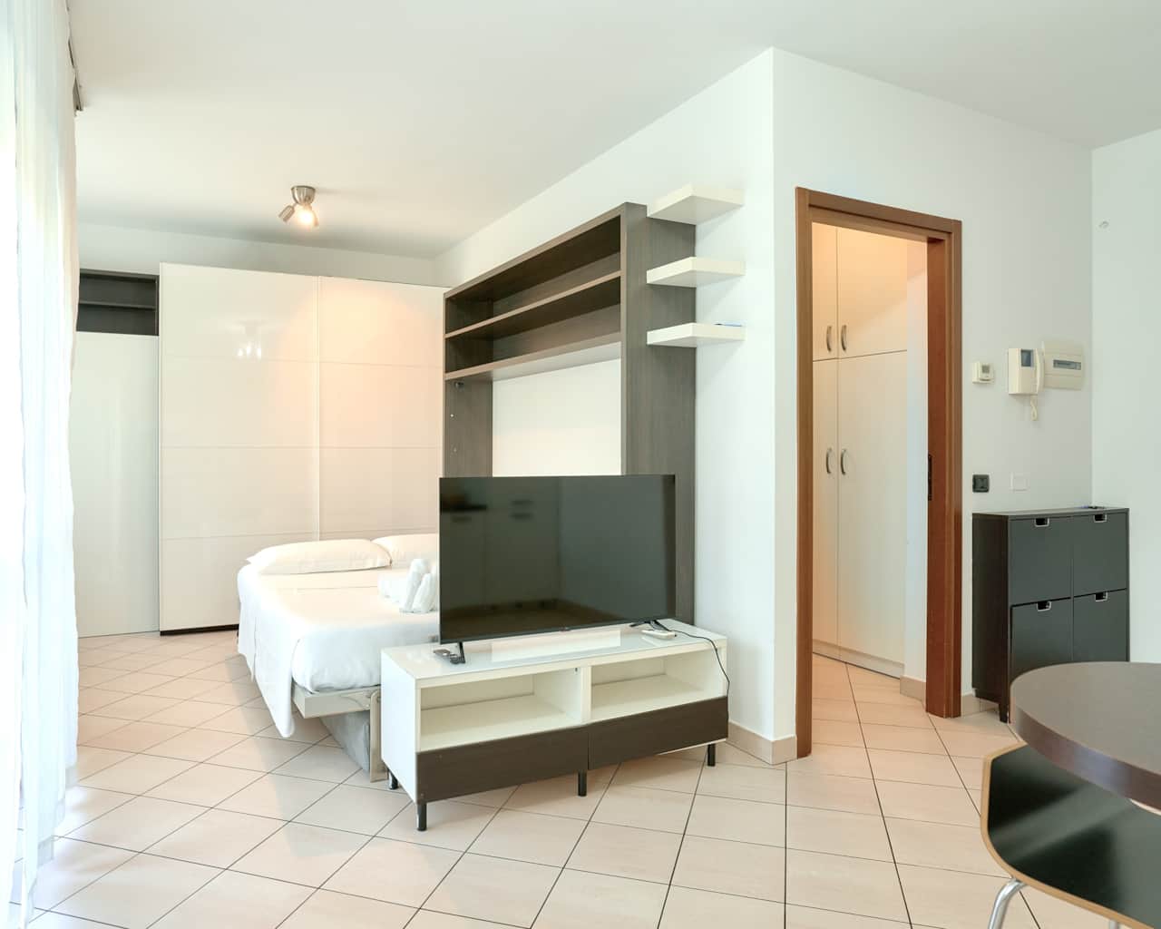Dormitorio con cama blanca, televisor y estantes de pared