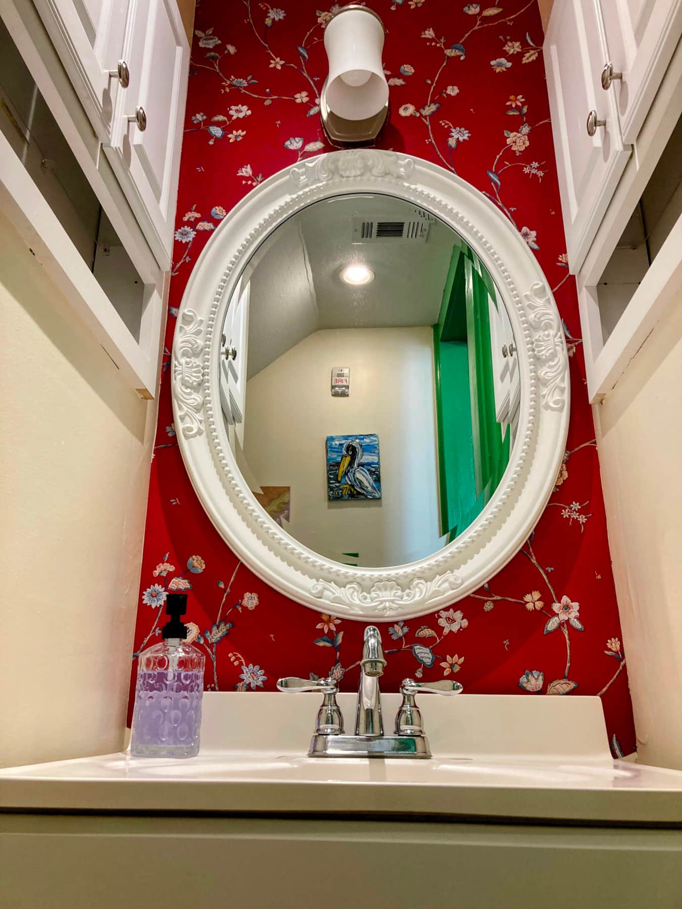 A bathroom sink with a round mirror and red floral wallpaper