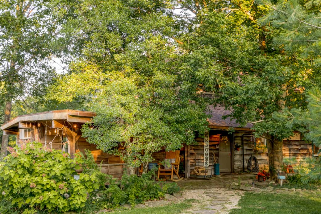 Warm evening light welcomes guests to the historic cabin beneath the trees