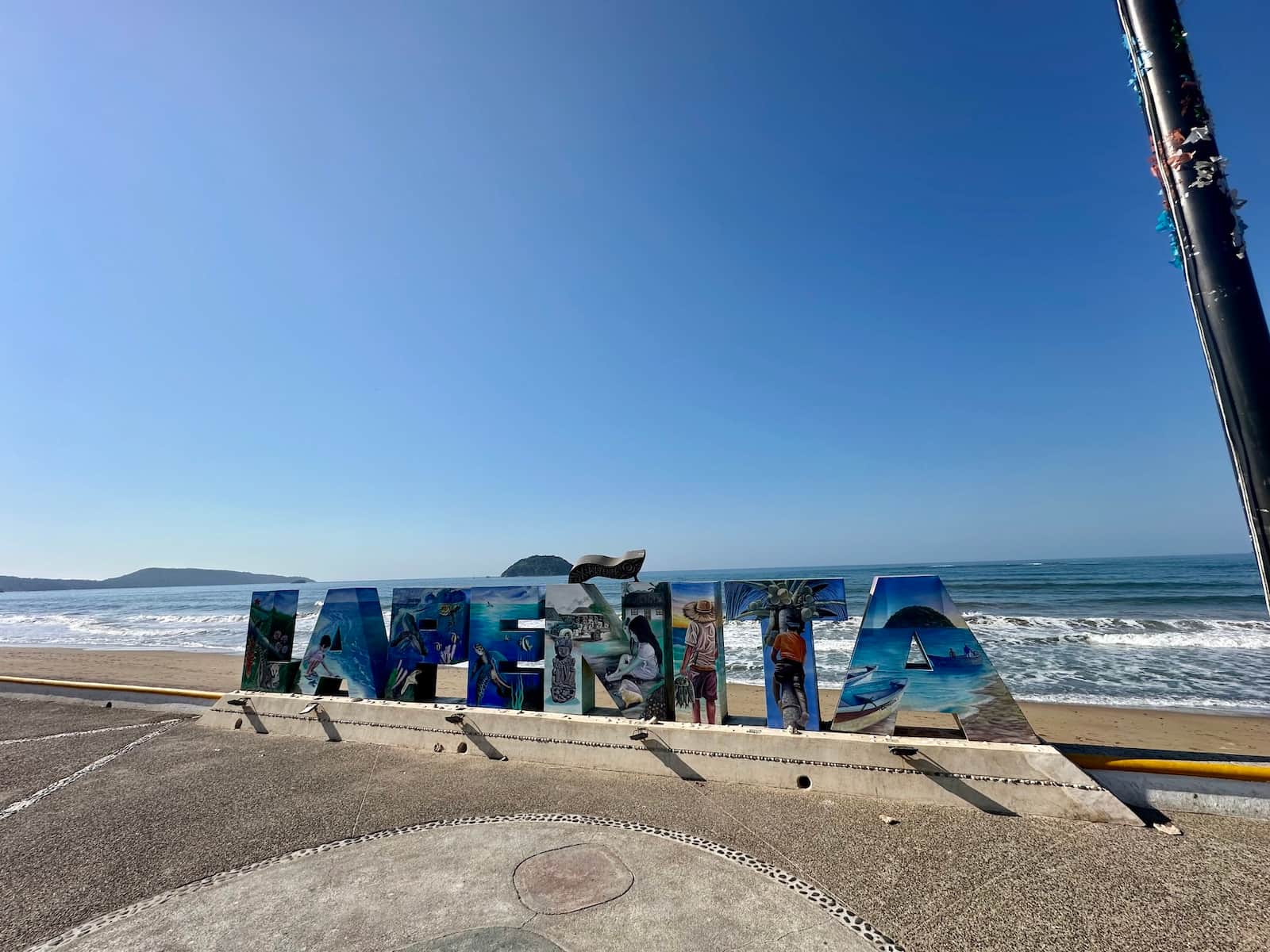 Painted La Penita letters on the malecon with the beach and Isla del Coral behind