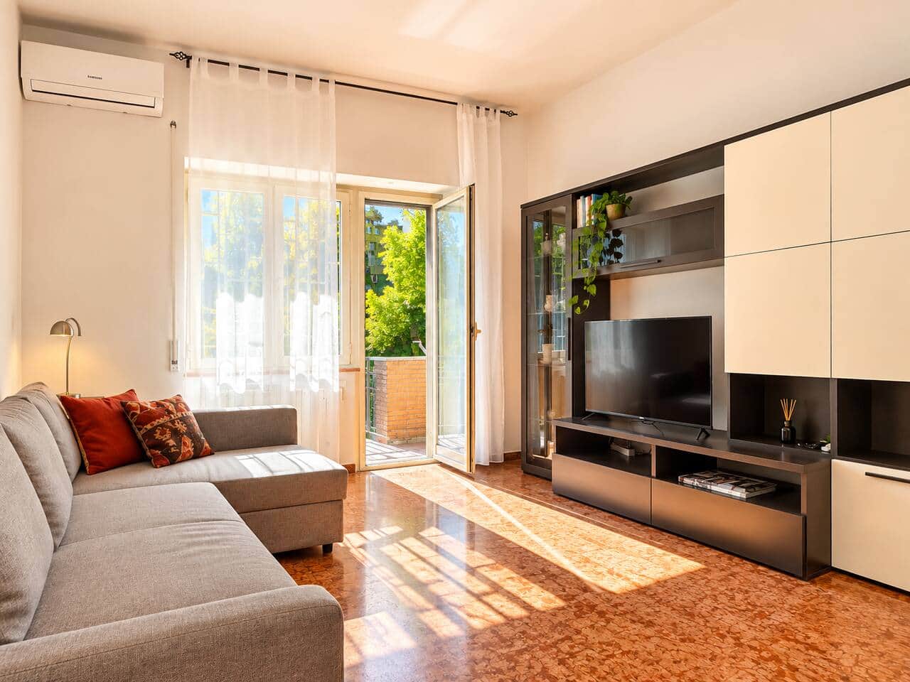 Soggiorno luminoso con divano, TV, aria condizionata e accesso diretto al balcone.
