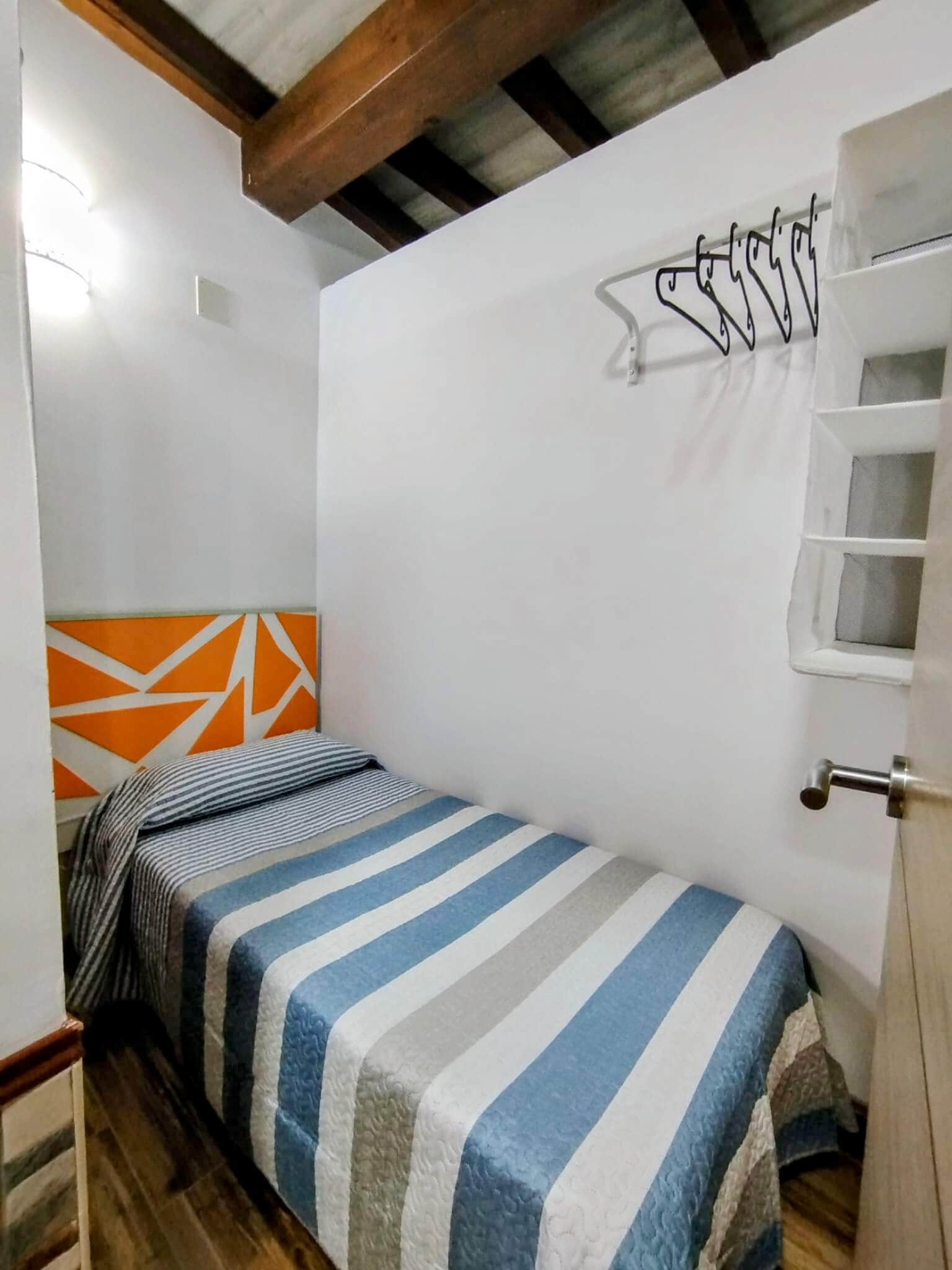 Dormitorio individual con cama de estilo moderno, cabecero decorativo geométrico y techo con vigas de madera