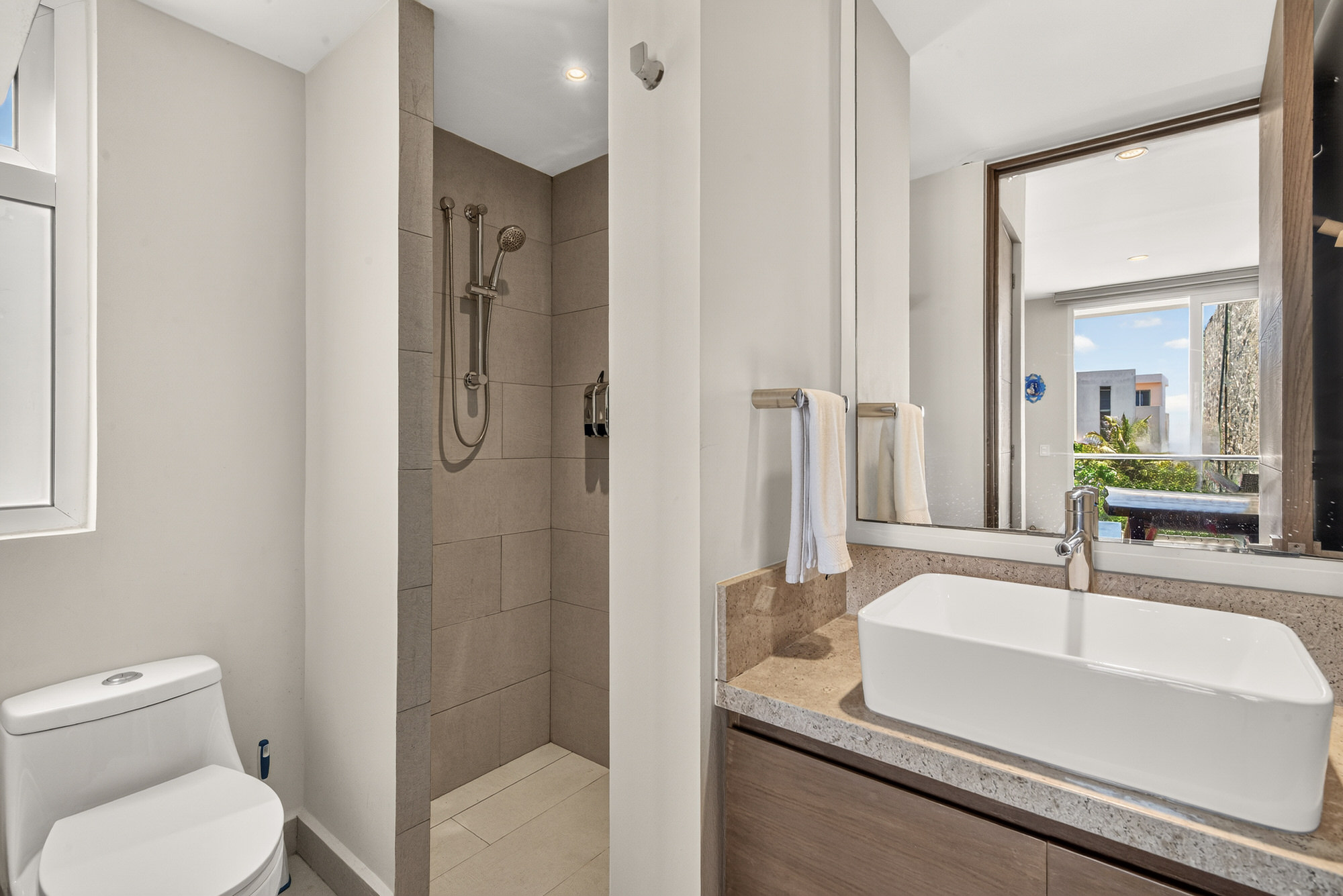 Modern bathroom with a walk-in shower, fresh towels, shampoo, conditioner, and body and hand soap.