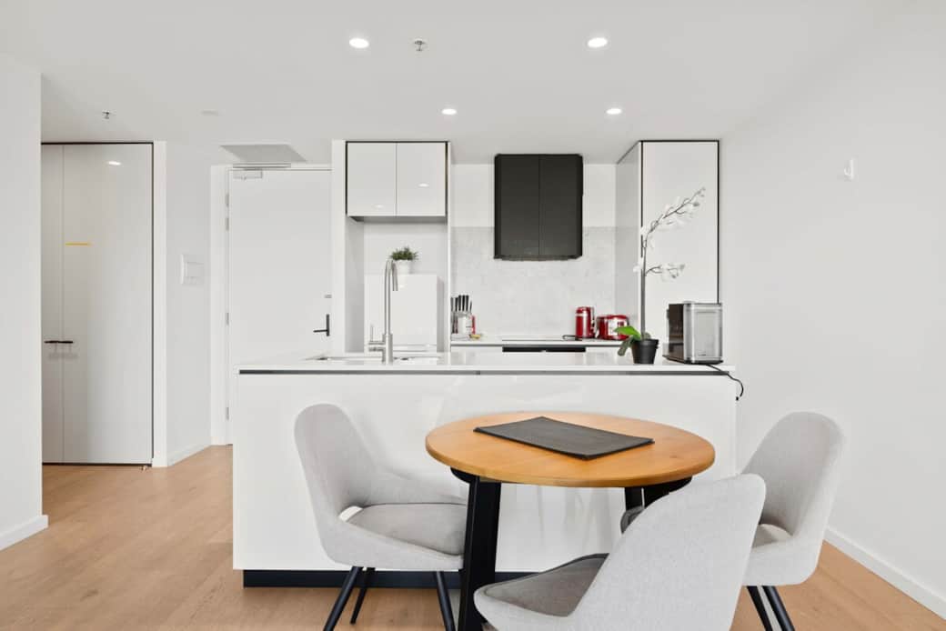 The  dining area is a study in modern elegance. White cabinetry and a sleek island with a sink create a functional cooking space. The dining table with well-designed chairs is ideal for meals, with a view of the kitchen that makes dining a pleasure.