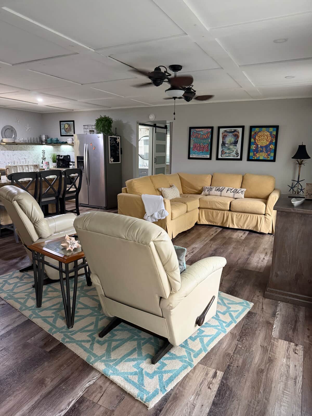 Inviting open-concept living space featuring cozy sectional seating, comfortable recliners over a bright teal pattern rug, and wood-grain floors. Adjacent to a kitchen breakfast bar, creating an open layout for gathering. 