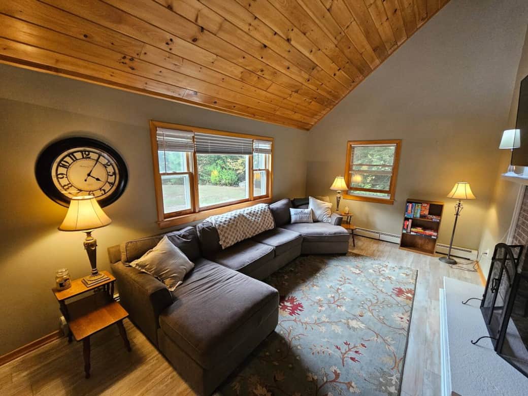 Relax in this inviting living room with soaring wood ceilings, oversized windows, and a plush sectional. Gather by the fireplace, enjoy the 65” TV, or unwind with board games on the cozy rug—perfect for families after a day in the White Mountains.