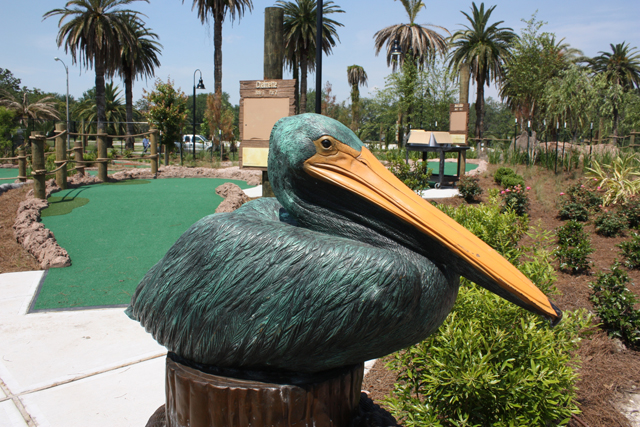 A large pelican statue sits in front of a mini golf course with palm trees in the background.