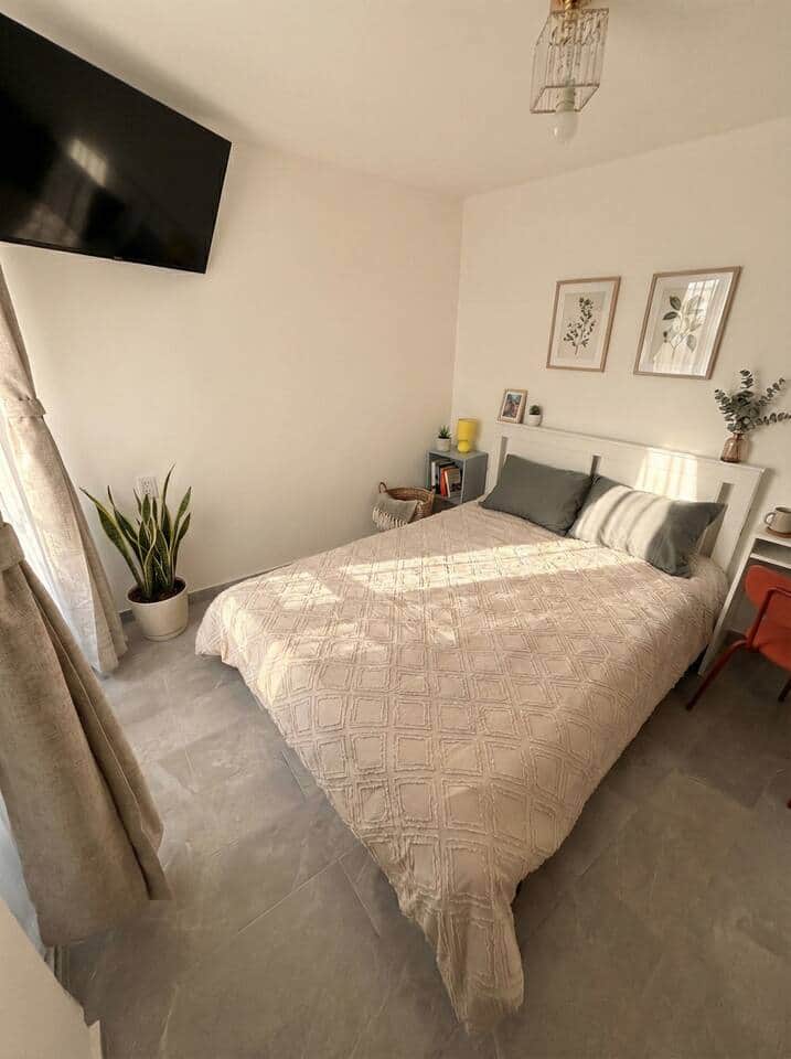 Cozy double bedroom with fresh linens, wall-mounted flat-screen TV, and warm natural light. Minimalist style, modern tile flooring, and soothing details for a clean, relaxing stay near everything Cozy double bedroom with fresh linens, wall-mounted flat-screen TV, and warm natural light. Minimalist style, modern tile flooring, and soothing details for a clean, relaxing stay near everything