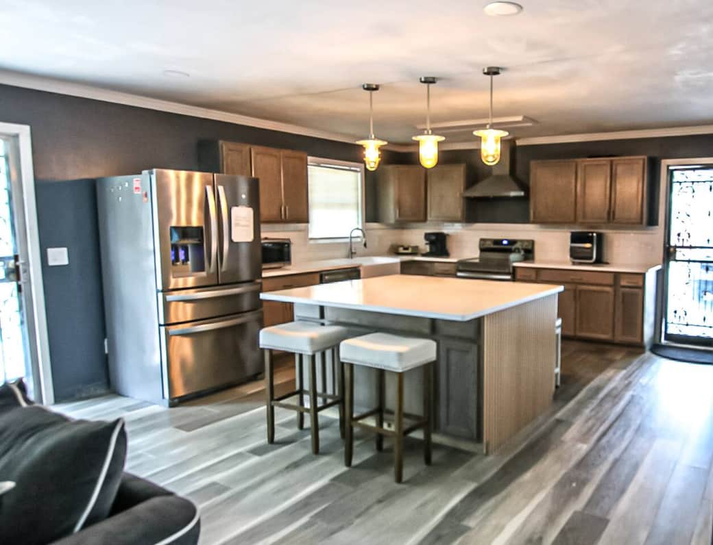 A colossal quartz island with plush upholstered stools creates the ultimate gathering spot. Warm wood cabinets and stainless appliances shine under amber pendant lights, while airy French doors flood this open-plan kitchen with natural light. A colossal quartz island with plush upholstered stools creates the ultimate gathering spot. Warm wood cabinets and stainless appliances shine under amber pendant lights, while airy French doors flood this open-plan kitchen with natural light.