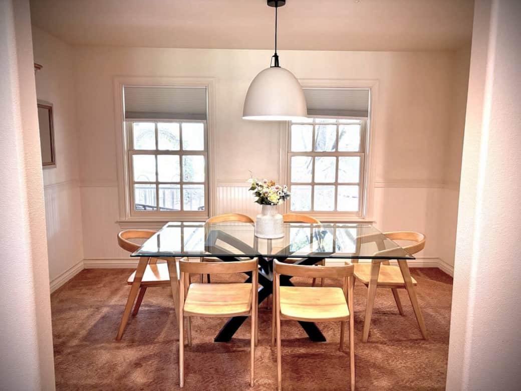 Inviting dining area with glass-top table and six yellow mid-century chairs with a white dome pendant light.  