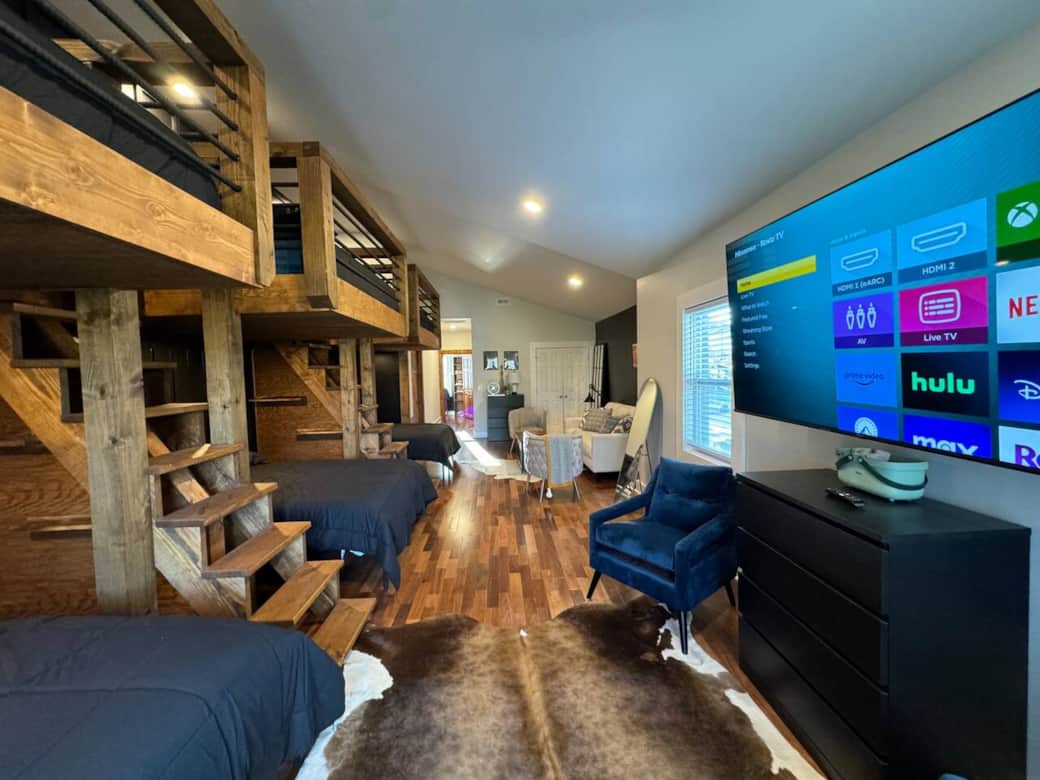this spacious bedroom is ideal for accommodating groups. The TV adds entertainment, while the room's chic decor and window let in natural light, creating a pleasant and comfortable ambiance.