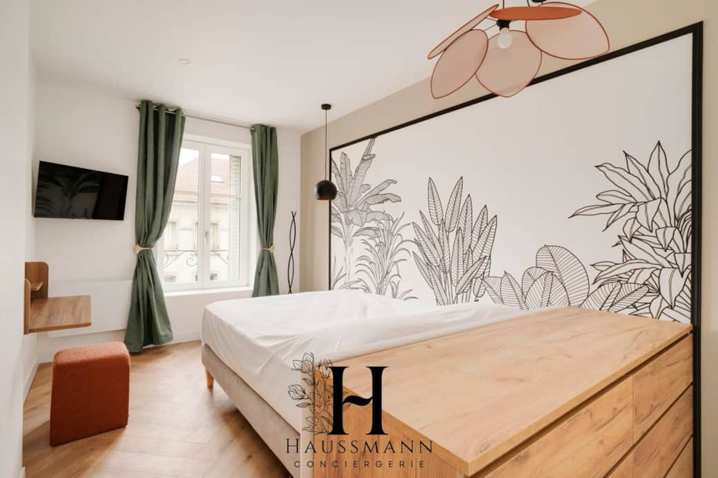 Chambre élégante avec lit double confortable et literie de qualité, TV murale et rangements.  Décoration soignée et coin bureau pratique, idéal pour travailler ou se détendre dans un cadre lumineux et apaisant.
