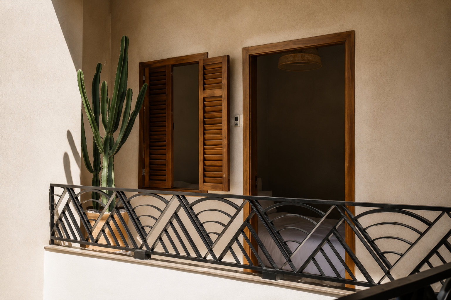 La coursive du premier étage. Garde-corps en ferronnerie Art déco, volets de bois, cactus. La galerie qui distribue les chambres autour du patio.