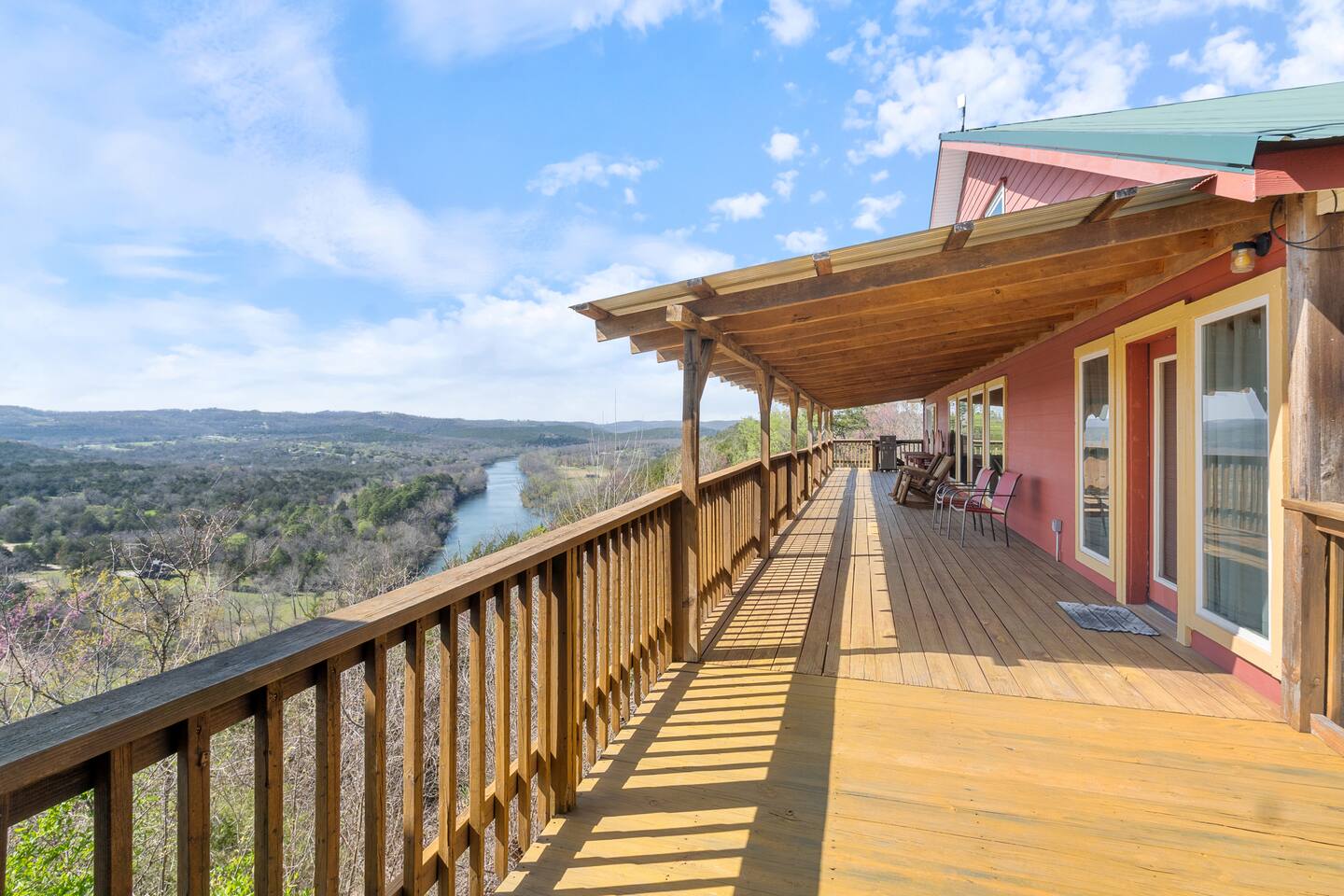 A wooden deck with a railing overlooking a scenic landscape with a river and mountains in the distance.