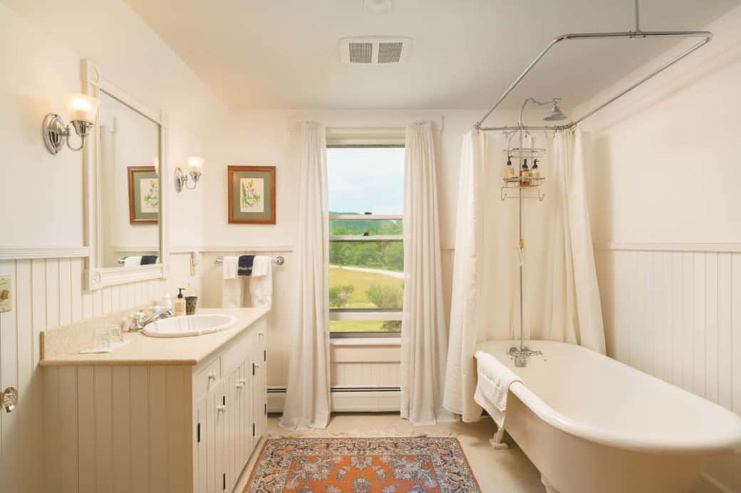 White bathroom with claw-foot tub by the window, inviting you to relax with views of Vermont’s lands