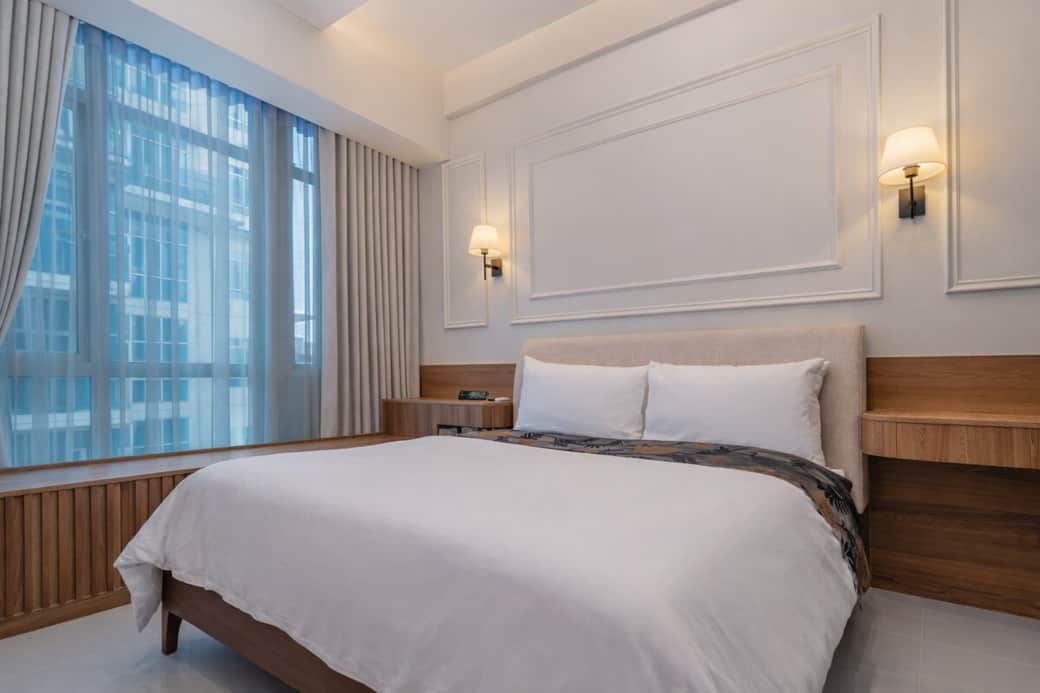 Elegant modern French-inspired bedroom with bespoke mouldings, warm wood accents, designer lighting, and a plush upholstered bed. Bright and refined, it offers a boutique-hotel feel in the heart of BGC.