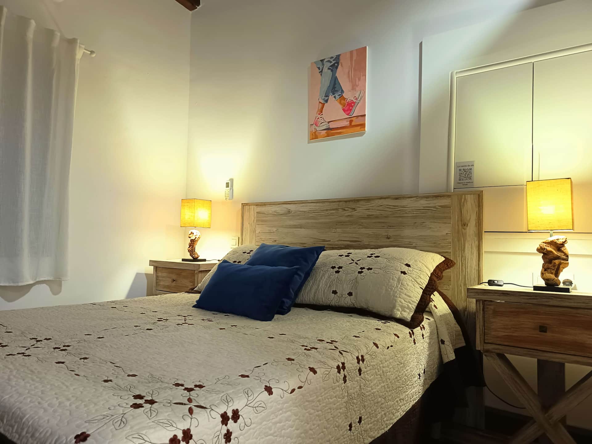 Dormitorio acogedor con cama de cabecero de madera, colcha floral en tonos crema y cojines decorativos