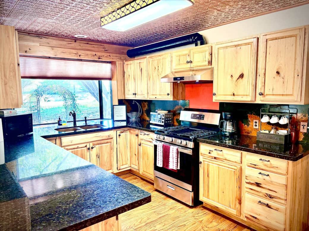 Bright and welcoming kitchen with abundant natural light, granite countertops, modern appliances, rustic cabinetry, and a distinctive copper-tin ceiling. Bright and welcoming kitchen with abundant natural light, granite countertops, modern appliances, rustic cabinetry, and a distinctive copper-tin ceiling.