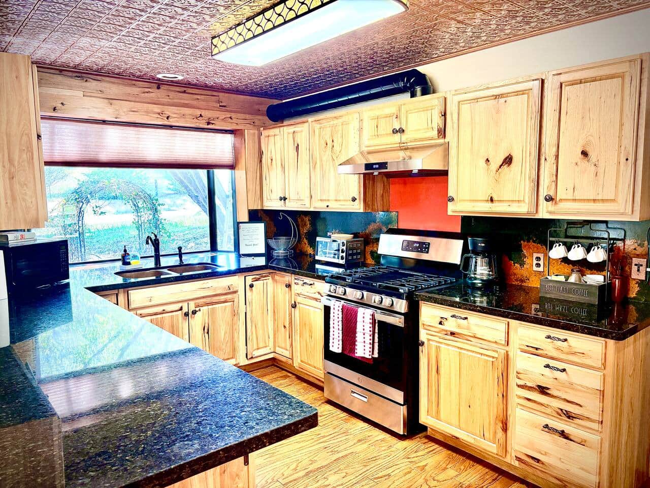 Bright and welcoming kitchen with abundant natural light, granite countertops, modern appliances, rustic cabinetry, and a distinctive copper-tin ceiling.