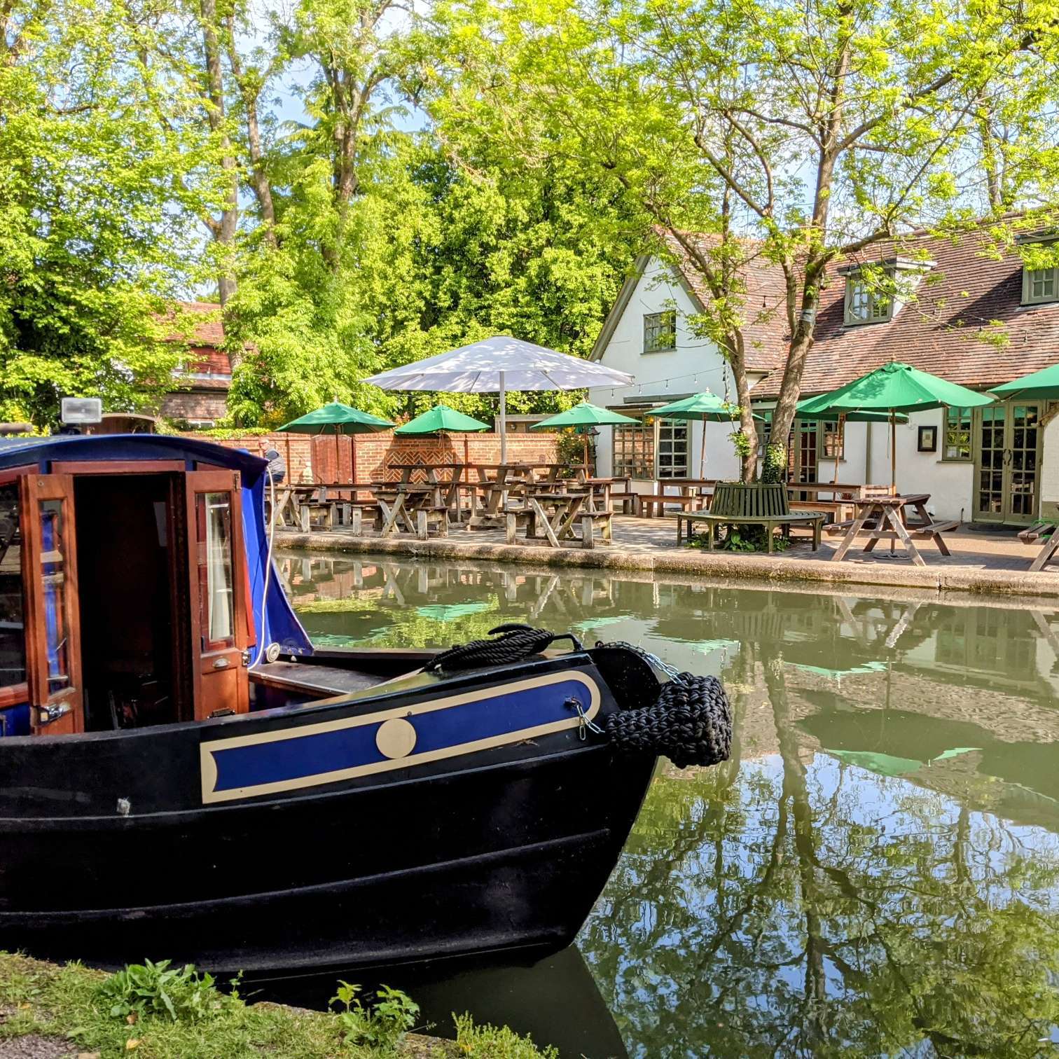 Canal boat bow in front of traditional canalside pub garden on the Grand Union in Hertfordshire