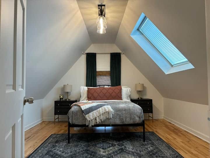 Charming loft bedroom with vaulted ceilings, a skylight for natural light, and cozy layered bedding