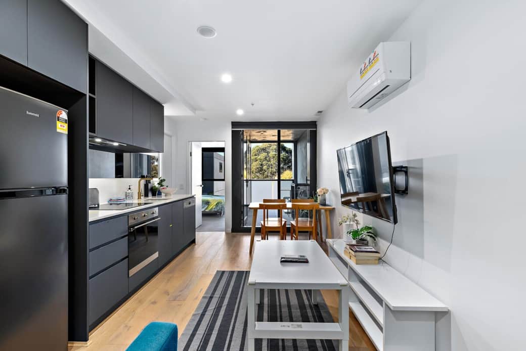 Step into a contemporary haven with this stylish living room. The blue sofa and white coffee table offer a cozy spot to unwind. Enjoy a meal at the wooden dining table or watch your favorite shows on the flat-screen TV. 