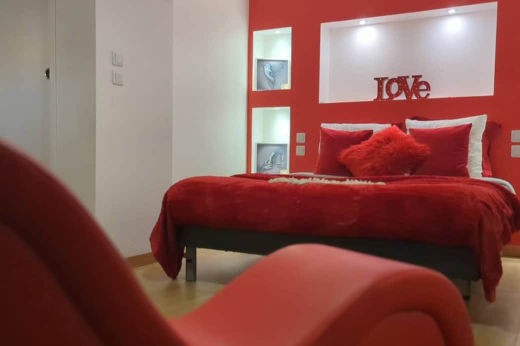 Un lit confortable avec une décoration rouge passion et une inscription 'LOVE' pour une ambiance chaleureuse. Des ports USB intégrés à la tête de lit permettent de charger vos appareils facilement.