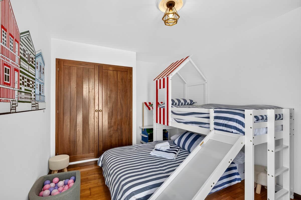 Playful Costa Nova room sleeping 3 with a fun house-themed bunk bed, built-in slide, and toys.