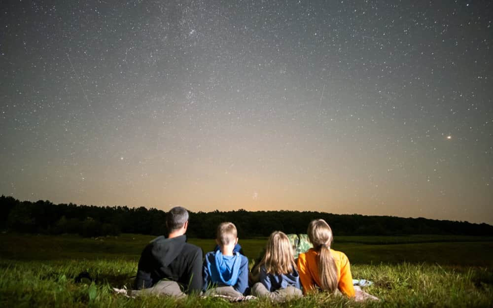 Family lying in a meadow gazing up at a starry night sky