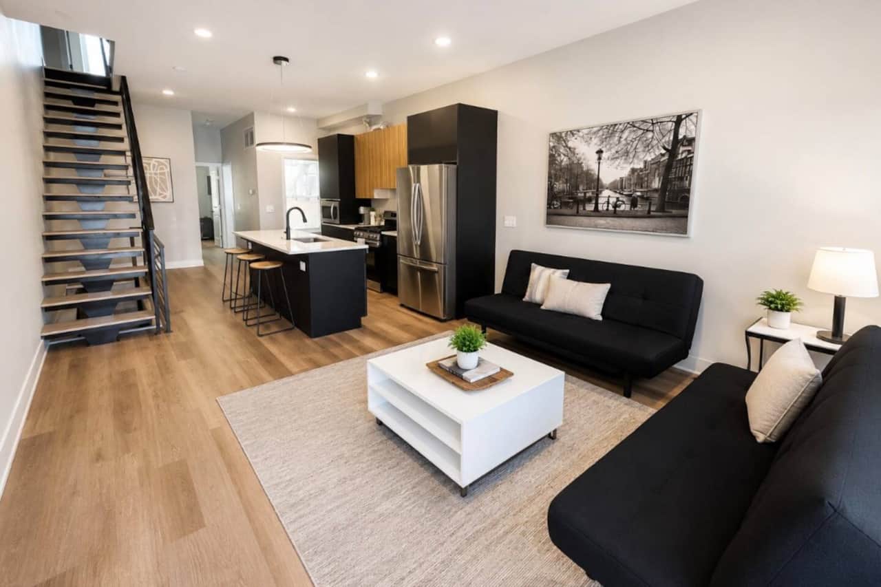 Living room featuring a large flat-screen TV and two comfortable futon sofa beds, providing extra sleeping space for guests. The room flows seamlessly into the fully equipped kitchen with an island and bar seating.