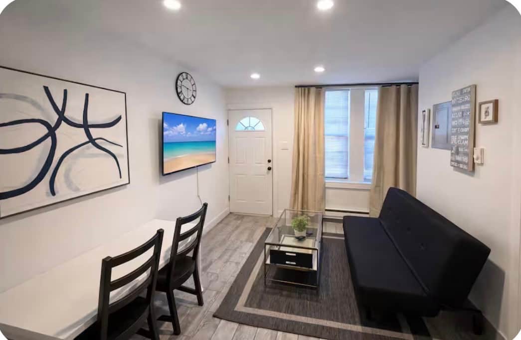 Modern Living Area with Futon Sofa BedRelax in this bright, modern living space featuring a comfortable futon sofa bed, smart TV, dining area, and plenty of natural light—perfect for lounging by day and a cozy night’s sleep.