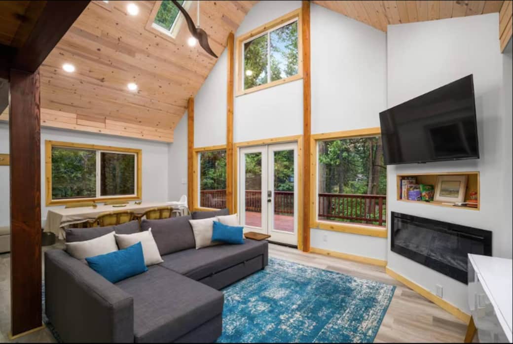 Stunning great room featuring floor-to-ceiling windows, warm wood accents, and a modern fireplace overlooking the forest.