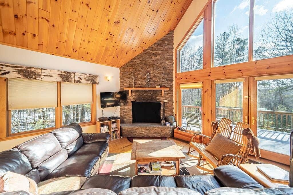 The living room features a soaring cathedral ceiling and a wall of windows that flood the space with natural light. Cozy up by the wood-burning fireplace, enjoy a movie night with Netflix, and stay comfortable year-round with air conditioning