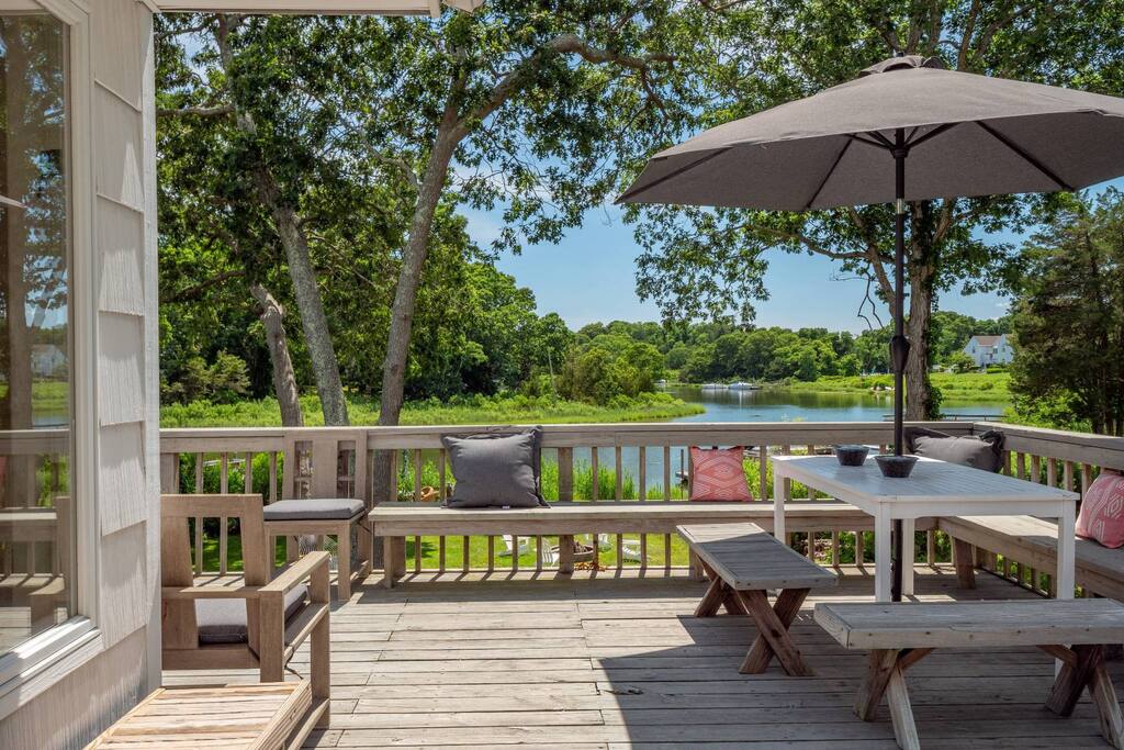 The deck with a long table, benches and an umbrella, looking over the water