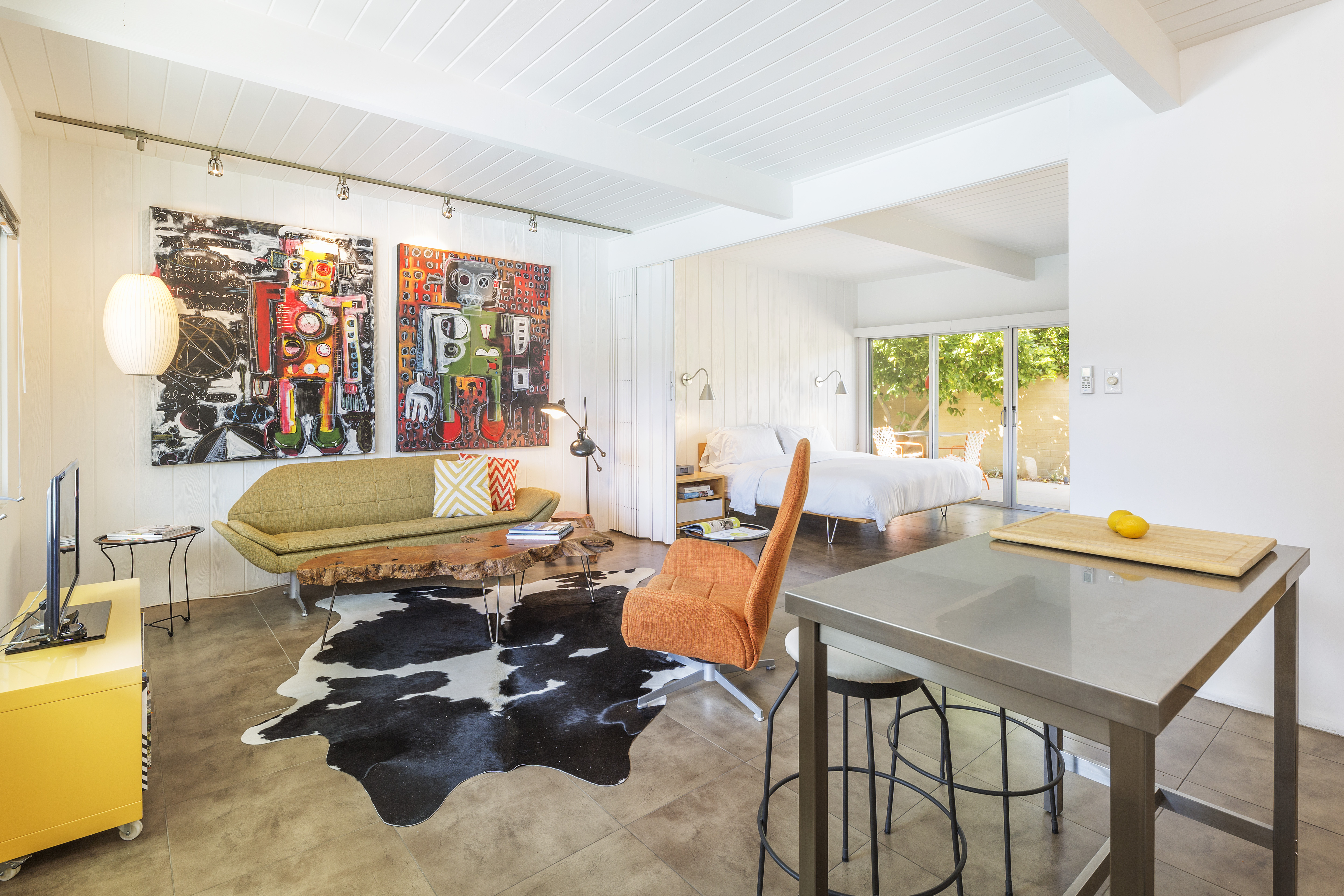 A wide view of a stylish suite with a sofa, dining table, chair, TV, and artwork.