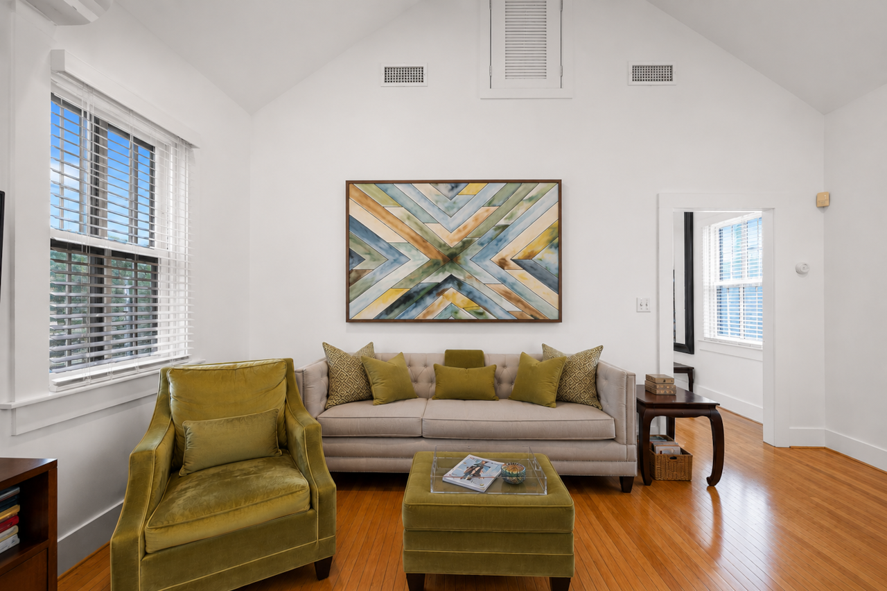 Living room with vaulted ceiling, wood floors, windows, and cozy seating.